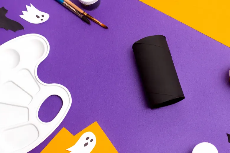 Black toilet paper roll laid out on crafts table next to paint palette