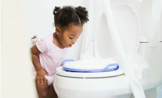 Entourée de papier hygiénique, une fillette regarde dans une cuvette de toilette.