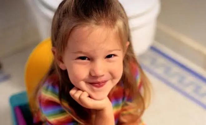 Une fillette souriante est assise sur son pot d'apprentissage de la propreté.
