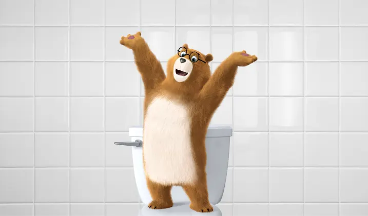 L'ours Dylan se tient fièrement debout sur la toilette, les bras levés bien haut.