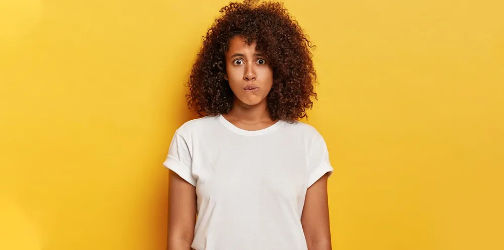 Mujer de cabello rizado de pie, sola, con cara de vergüenza