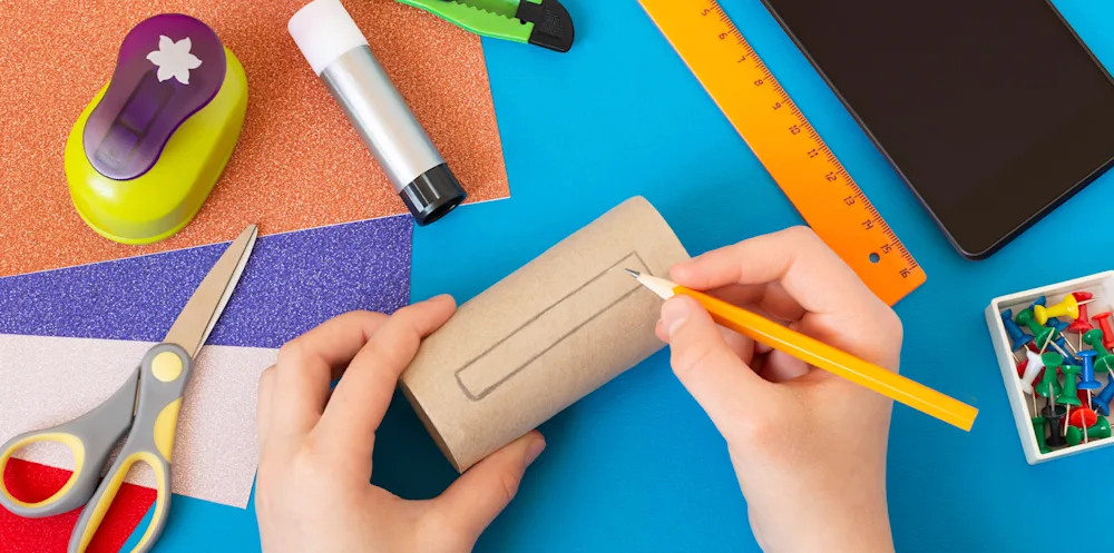 Primer plano de alguien que dibuja sobre papel higiénico con un escritorio rodeado de materiales para manualidades