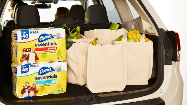 Paquetes de Charmin Essentials Strong y Essentials Soft en la cajuela de un auto con comestibles