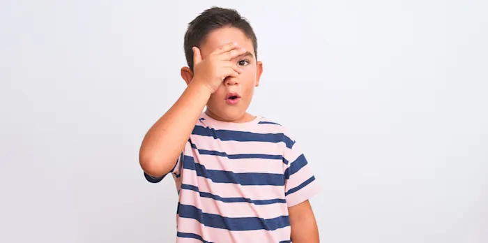 Un niño cubriéndose la cara con su mano