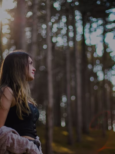 A young woman  with brown hairs standing in woods.