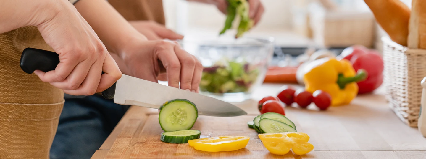 A person chopping cucumbers on a wooden cutting board.