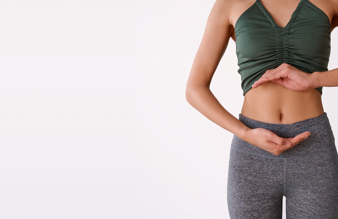 A woman standing with her hands resting on her lower abdomen.