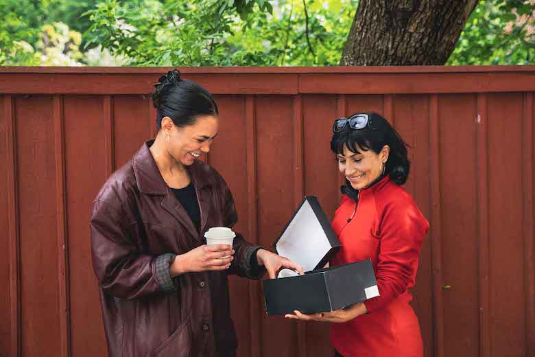 Två kvinnor tittar i kartong framför rött plank