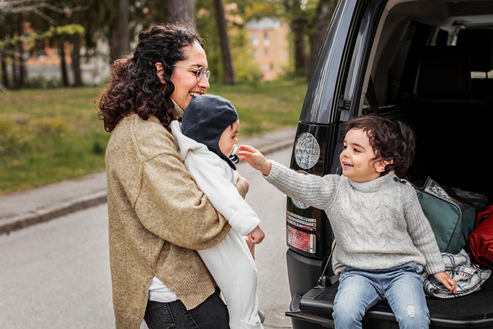 Mamma med två barn vid bakluckan av bil