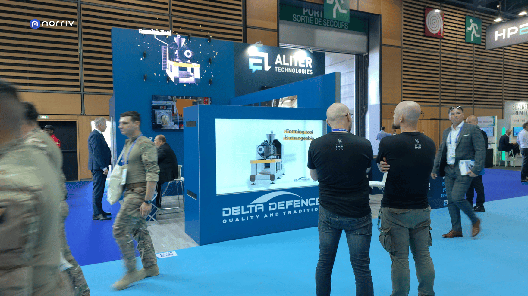 Visitors beside DELTA-DEFENCE's horizontal Hologram Box showing a 3D machine, with a holographic fan display above the booth.
