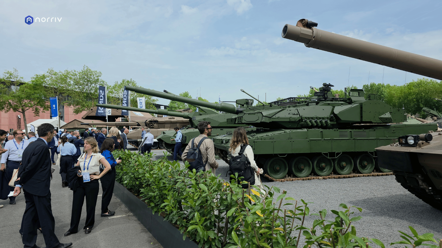 Visitors walking beside a row of full-size tanks in the outdoor exhibition area at Eurosatory 2026 in Paris.