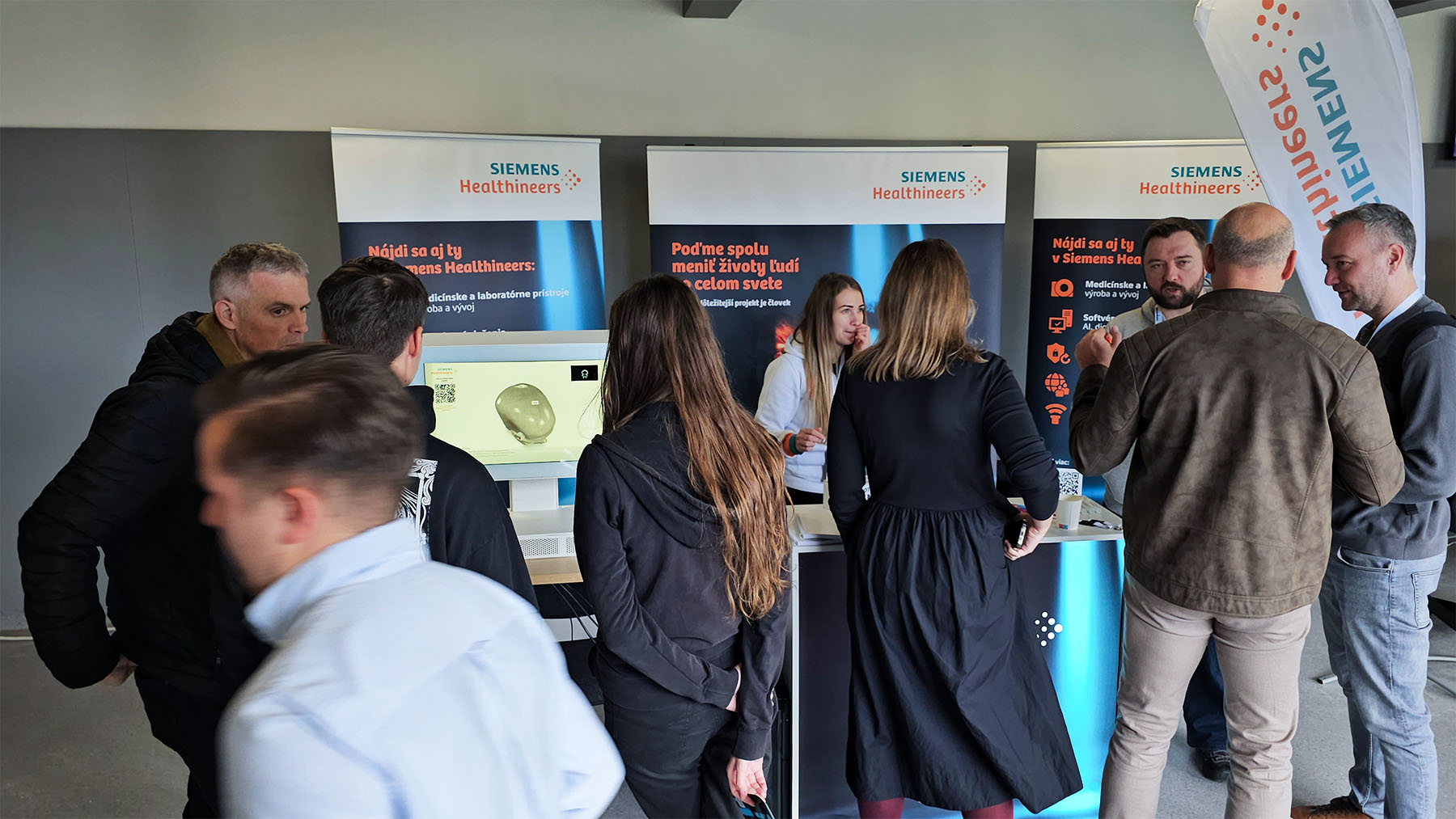 A group of people interact at a Siemens Healthineers booth featuring display banners and informational materials in a modern indoor space.