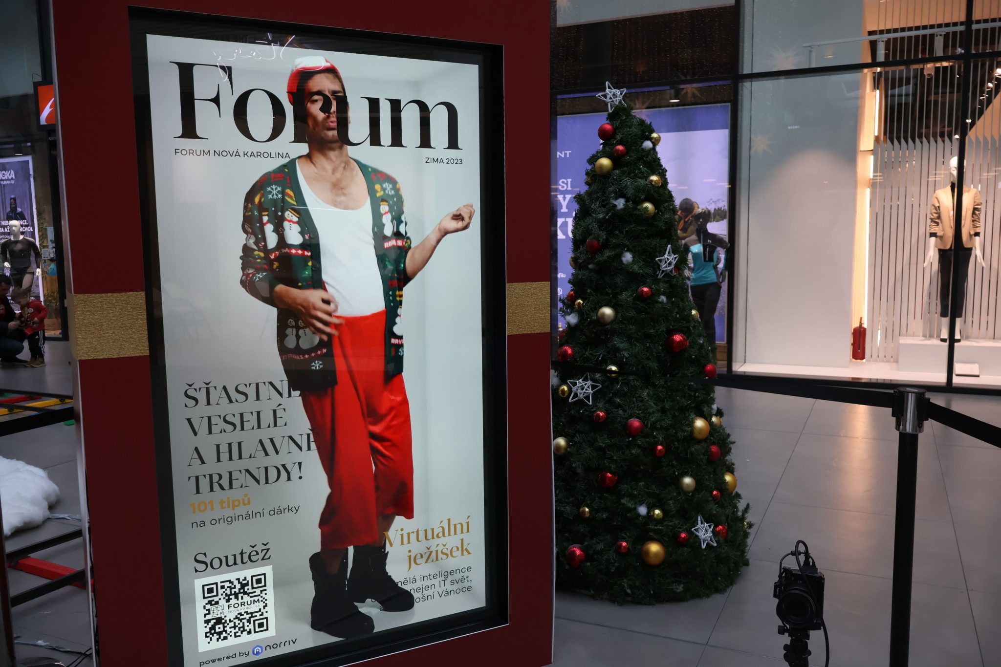 The norriv Hologram Box displays a magazine cover featuring a festive-dressed person beside a Christmas tree in a modern mall.