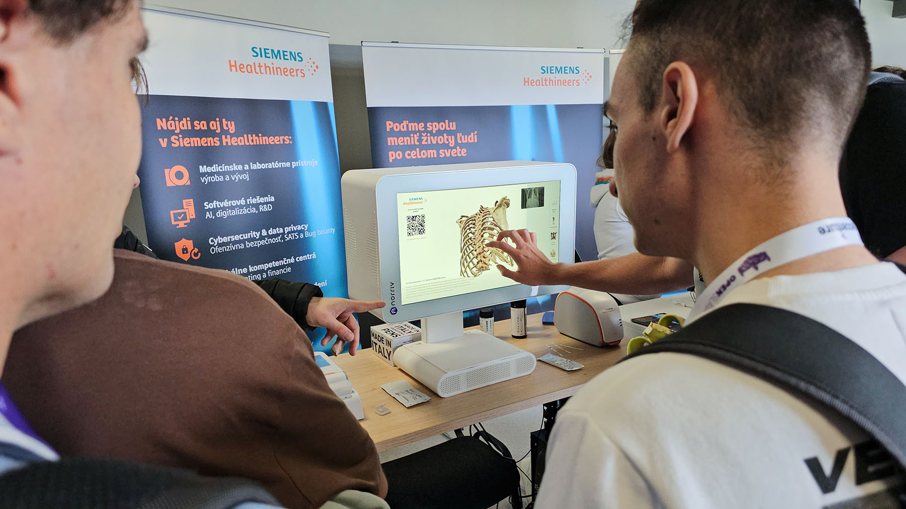 A person uses a touchscreen showing a 3D ribcage scan at the Siemens Healthineers booth, as others look on.
