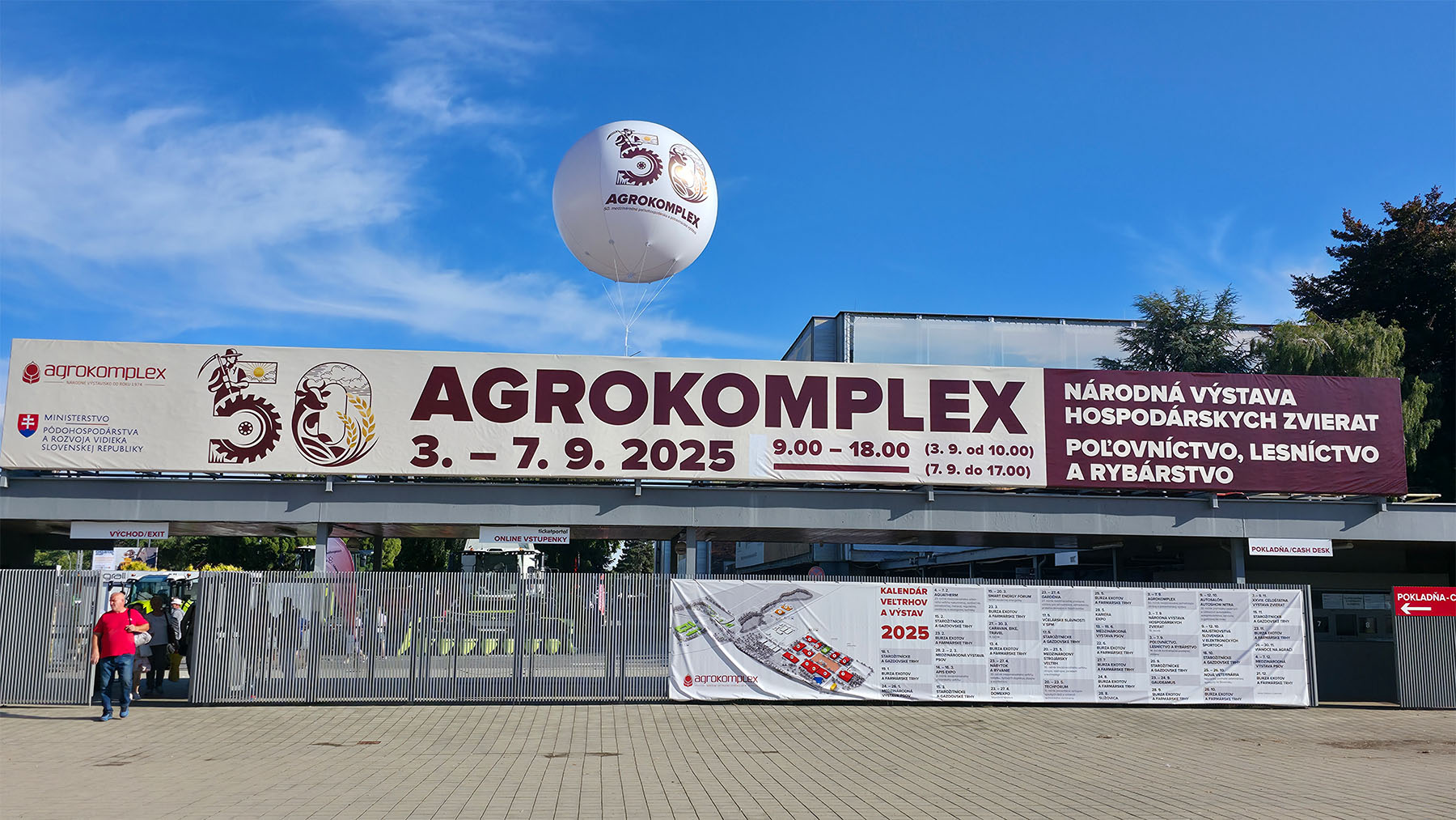 A large banner promotes the AGROKOMPLEX fair, Sept 3–7, 2025, at an outdoor Slovakia venue, event info in Slovak.