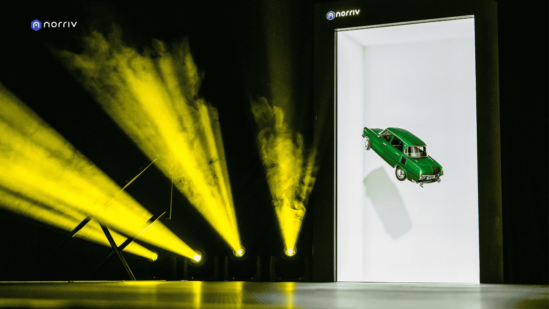 A green vintage car appears suspended vertically inside a bright, rectangular doorway, surrounded by dramatic yellow stage lights and haze, with the Norriv logo visible at the top and in the corner.