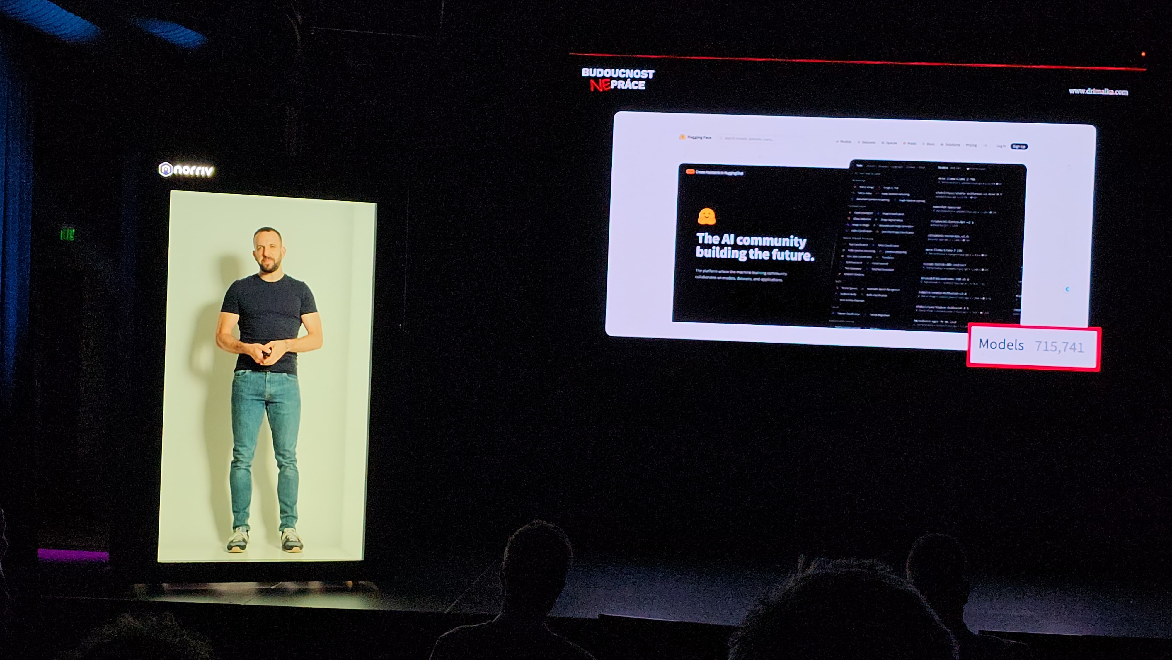 A man stands inside a vertical, illuminated display on stage, while a large screen beside him shows a website with the text Models: 715,741 highlighted in pink. Audience silhouettes are visible in the foreground.