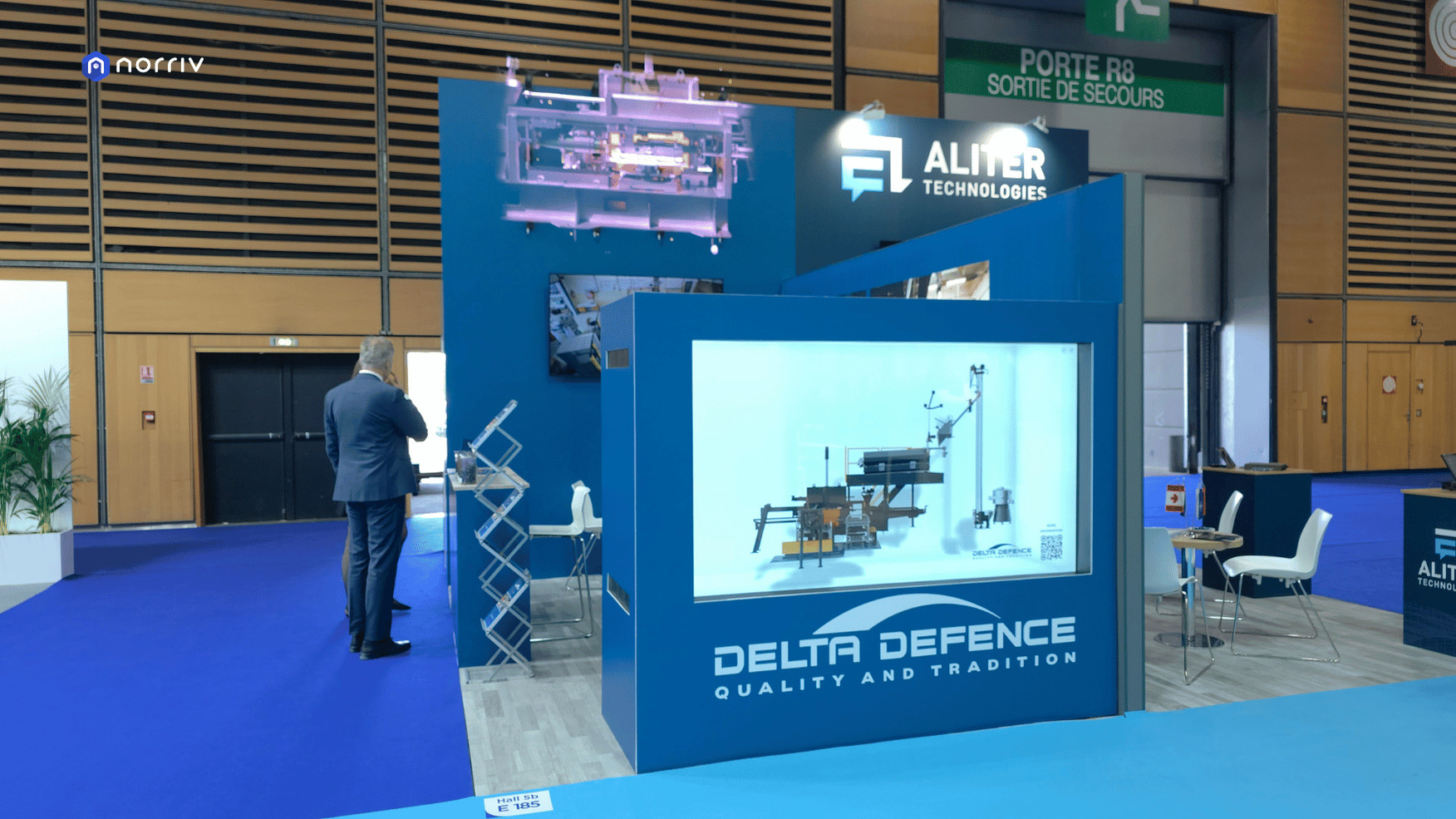 DELTA-DEFENCE's blue booth with a horizontal Hologram Box displaying industrial equipment and a purple holographic machine above.