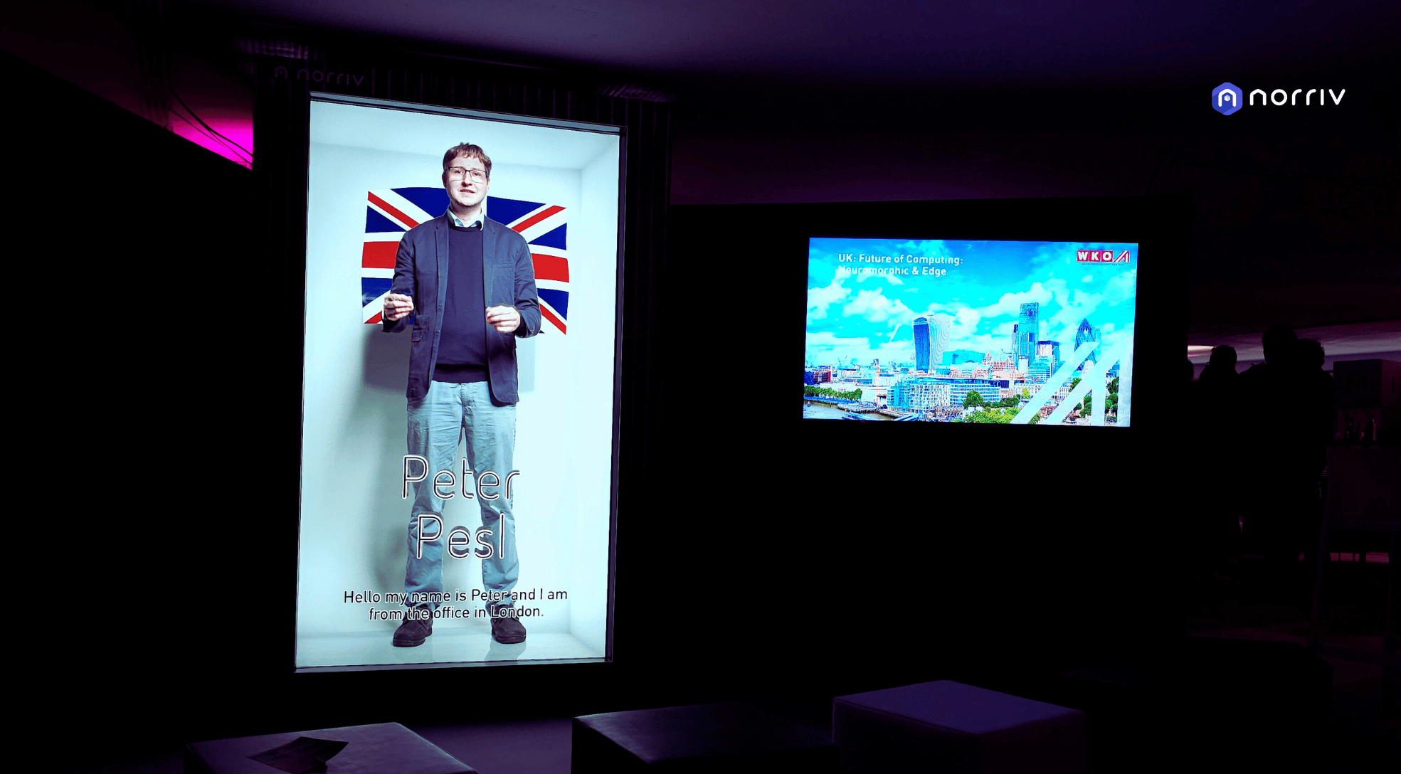 A large illuminated display shows a man standing in front of a Union Jack flag with text Peter Pest and a greeting. Next to it, a screen displays a cityscape with the UK flag and informational text.