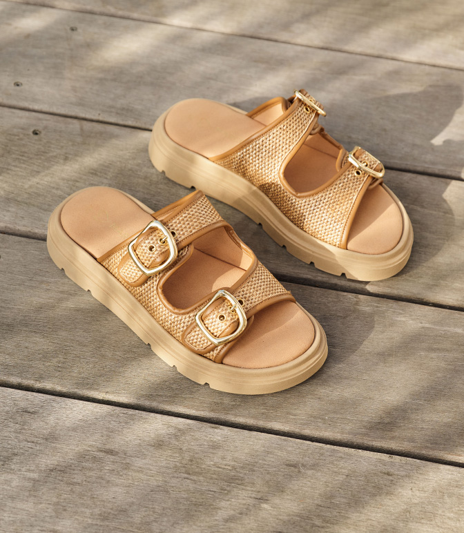 Sandali dorati con due fibbie su una base di legno grigia, suola beige con plateau, scarpa casual estiva