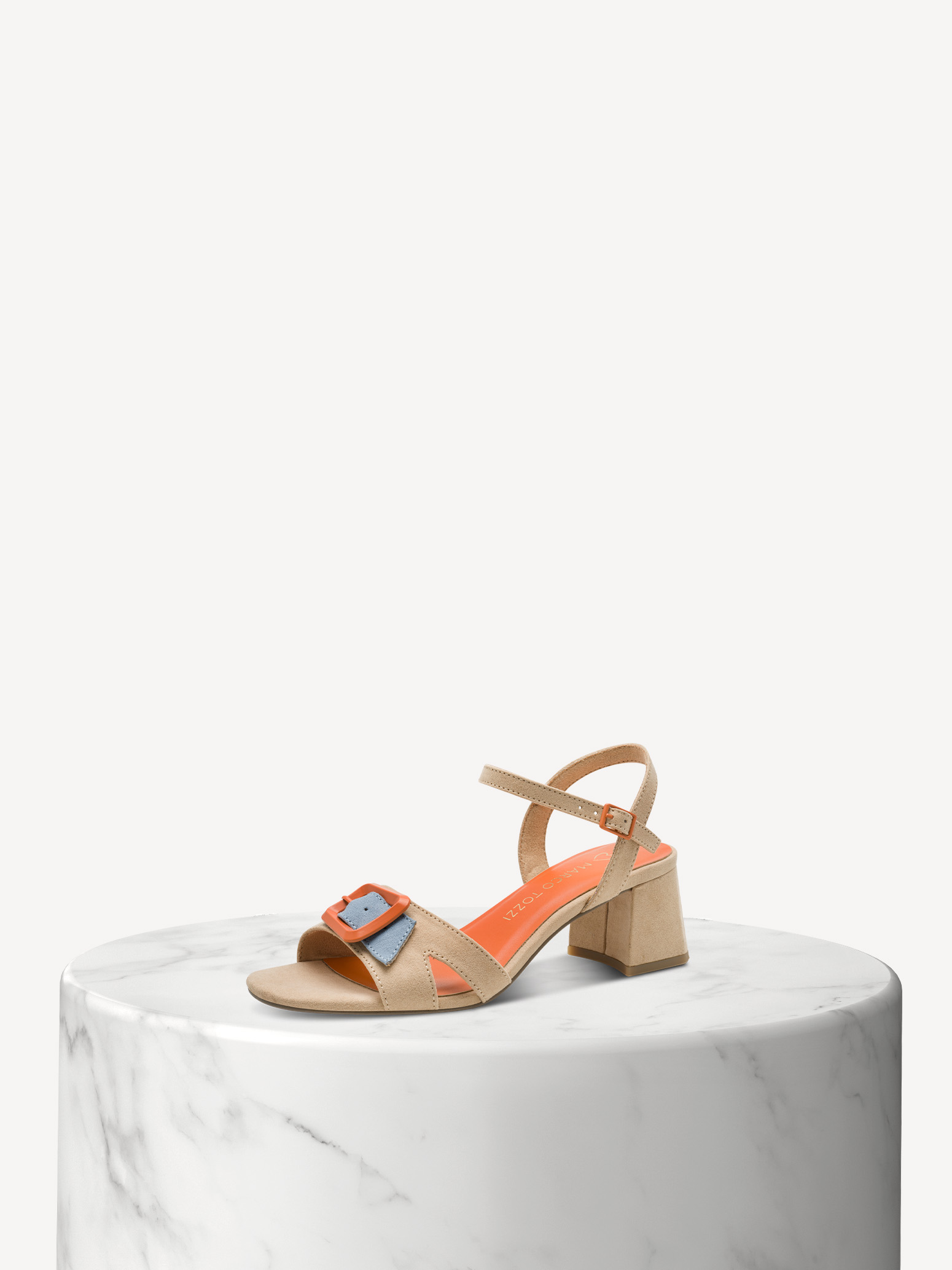 Sandalo beige con tacco a blocco e fibbie colorate su base di marmo bianco su sfondo chiaro