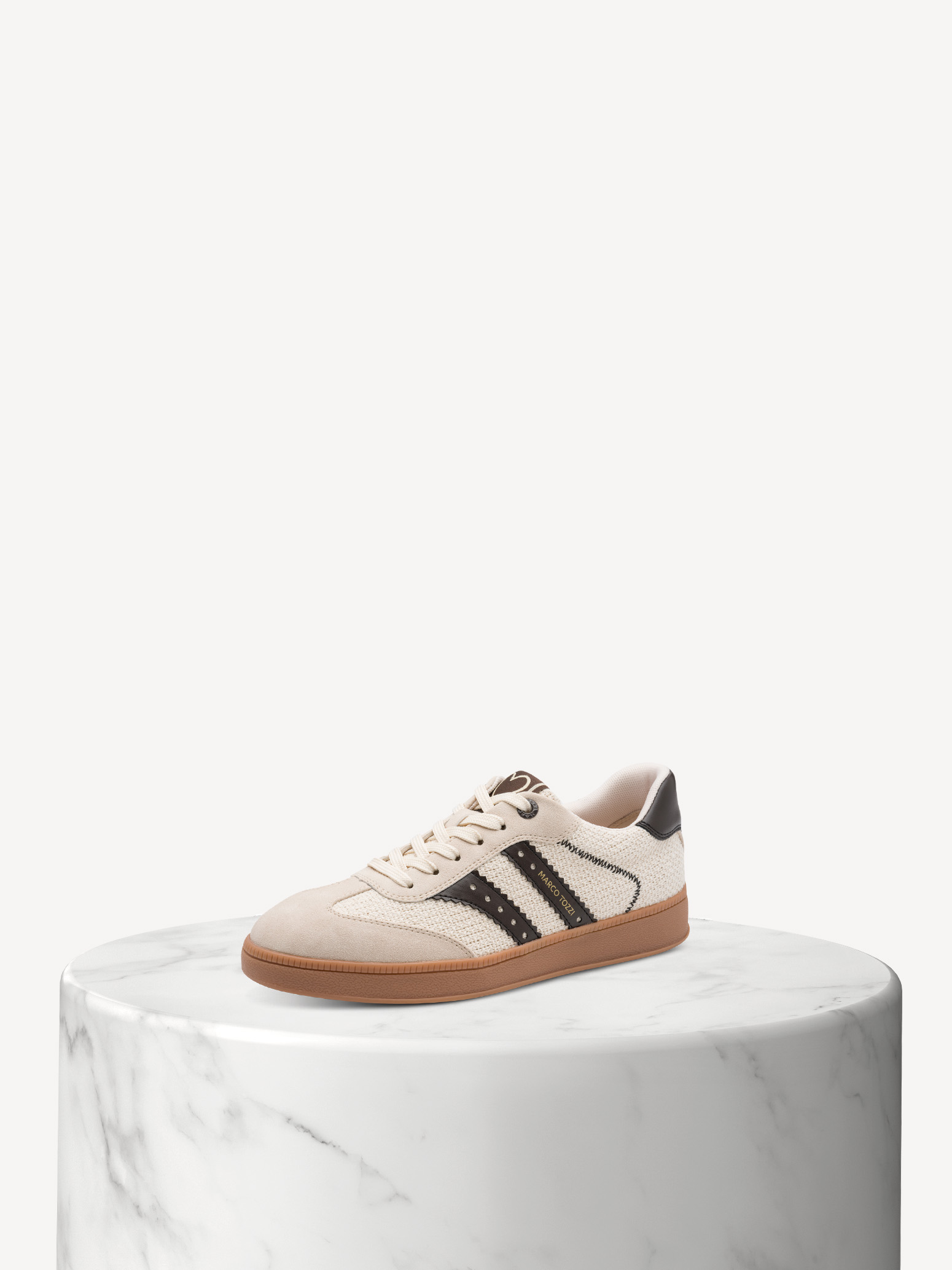 Beiger Sneaker mit schwarzem Streifen und brauner Sohle auf weißem Marmorsockel vor hellem Hintergrund.