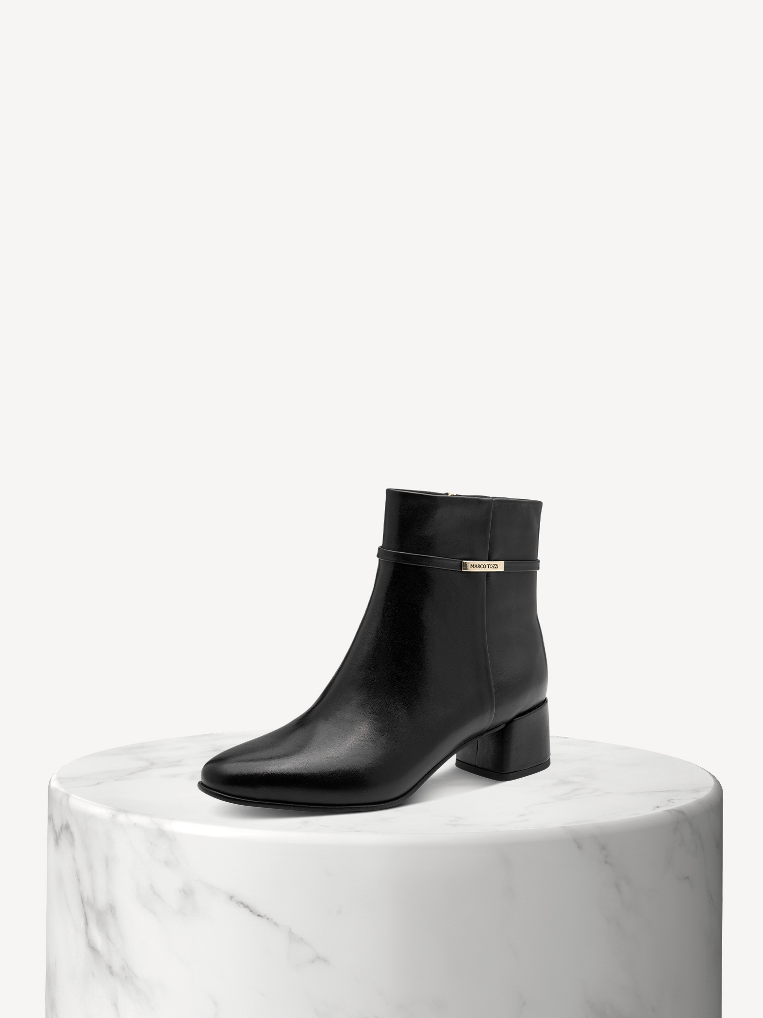 Black leather ankle boots with block heels on a white marble base against a light-colored background.