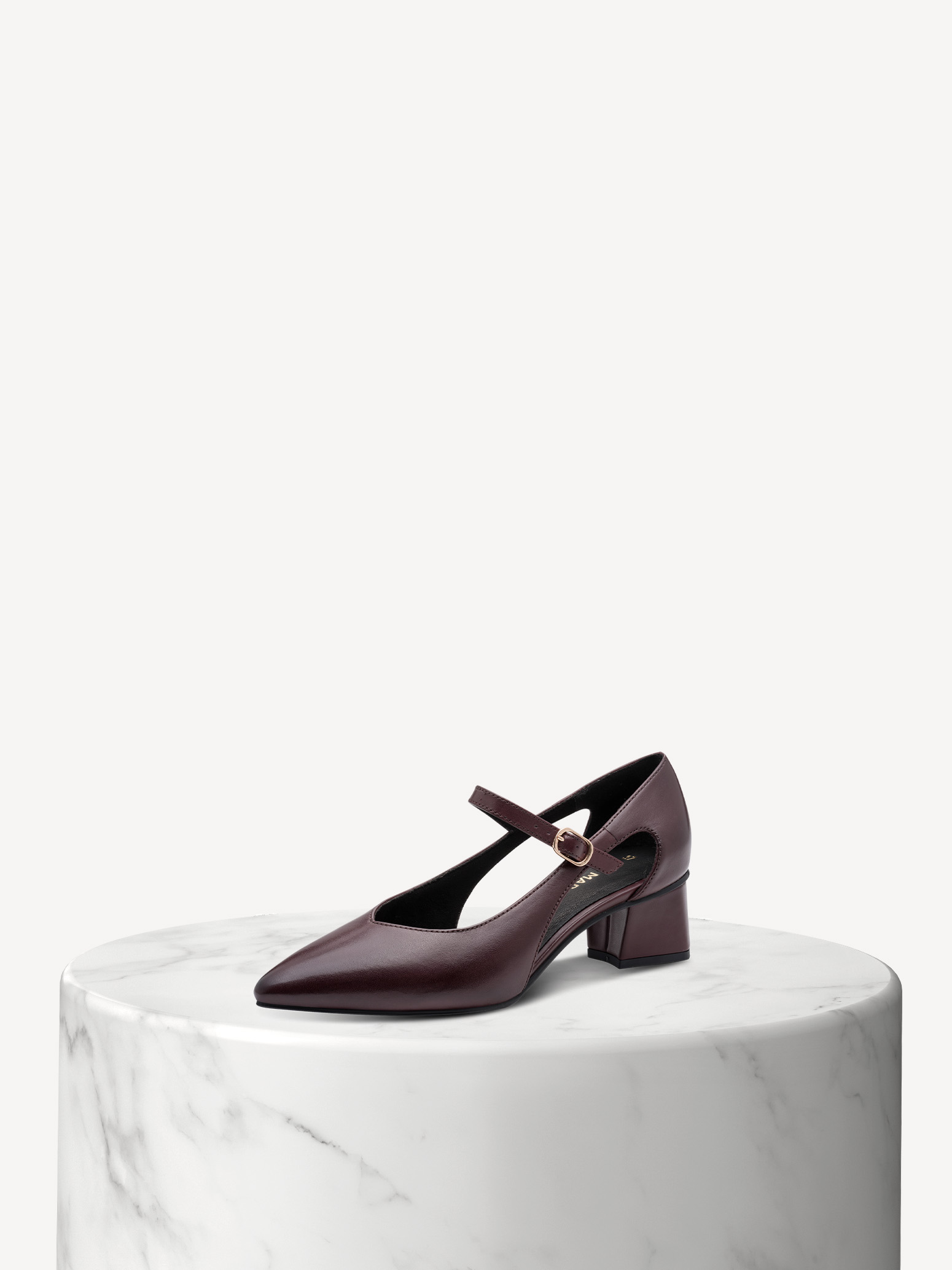 Dark brown leather pumps with straps and block heels on a white marble base against a light-colored background.