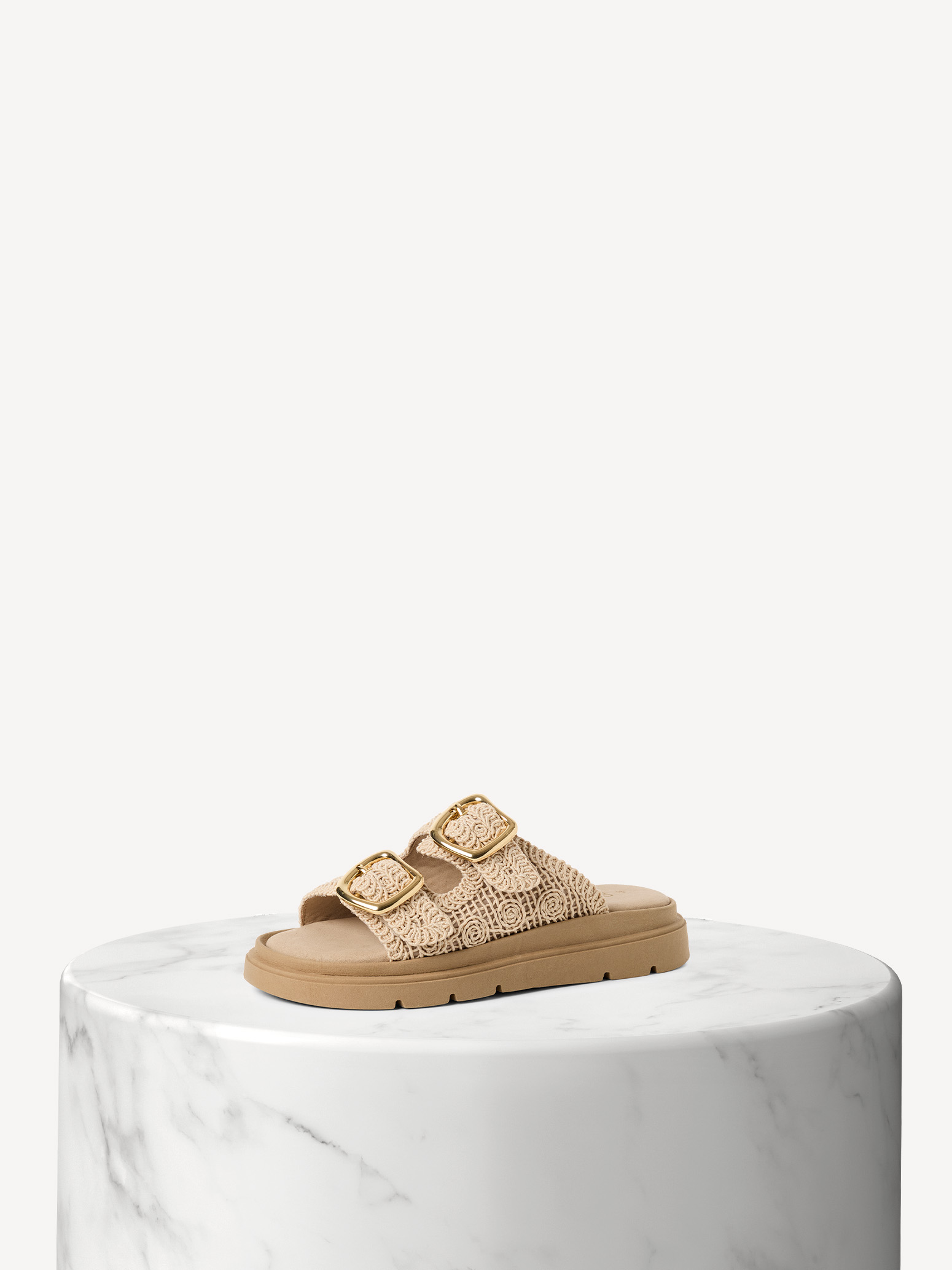 Sandalo beige con cinturini all'uncinetto e fibbie dorate su una base di marmo bianco su sfondo chiaro