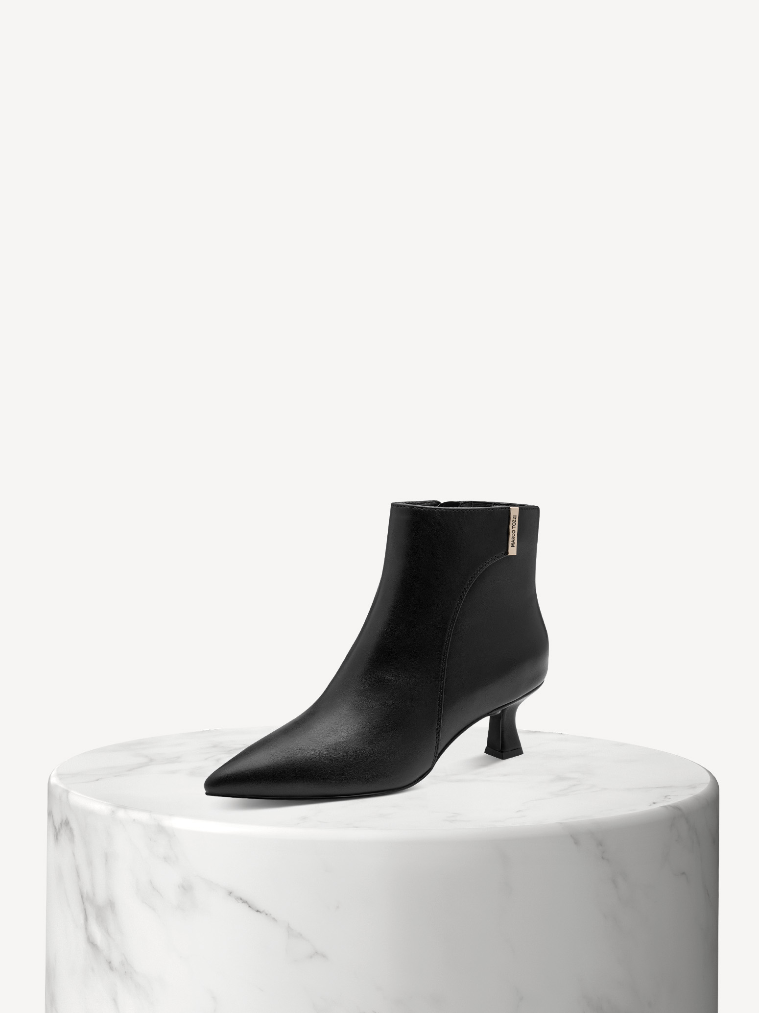 Stivaletto nero a punta con tacco kitten heel su una base di marmo bianco, su uno sfondo beige.