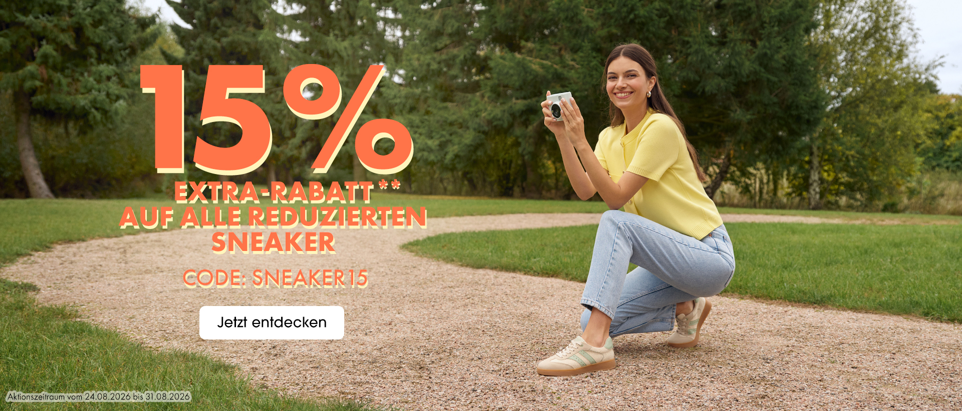 Frau in gelbem Shirt und Jeans hockt im Park mit Kamera, Werbung für 15% Extra-Rabatt auf reduzierte Sneaker.