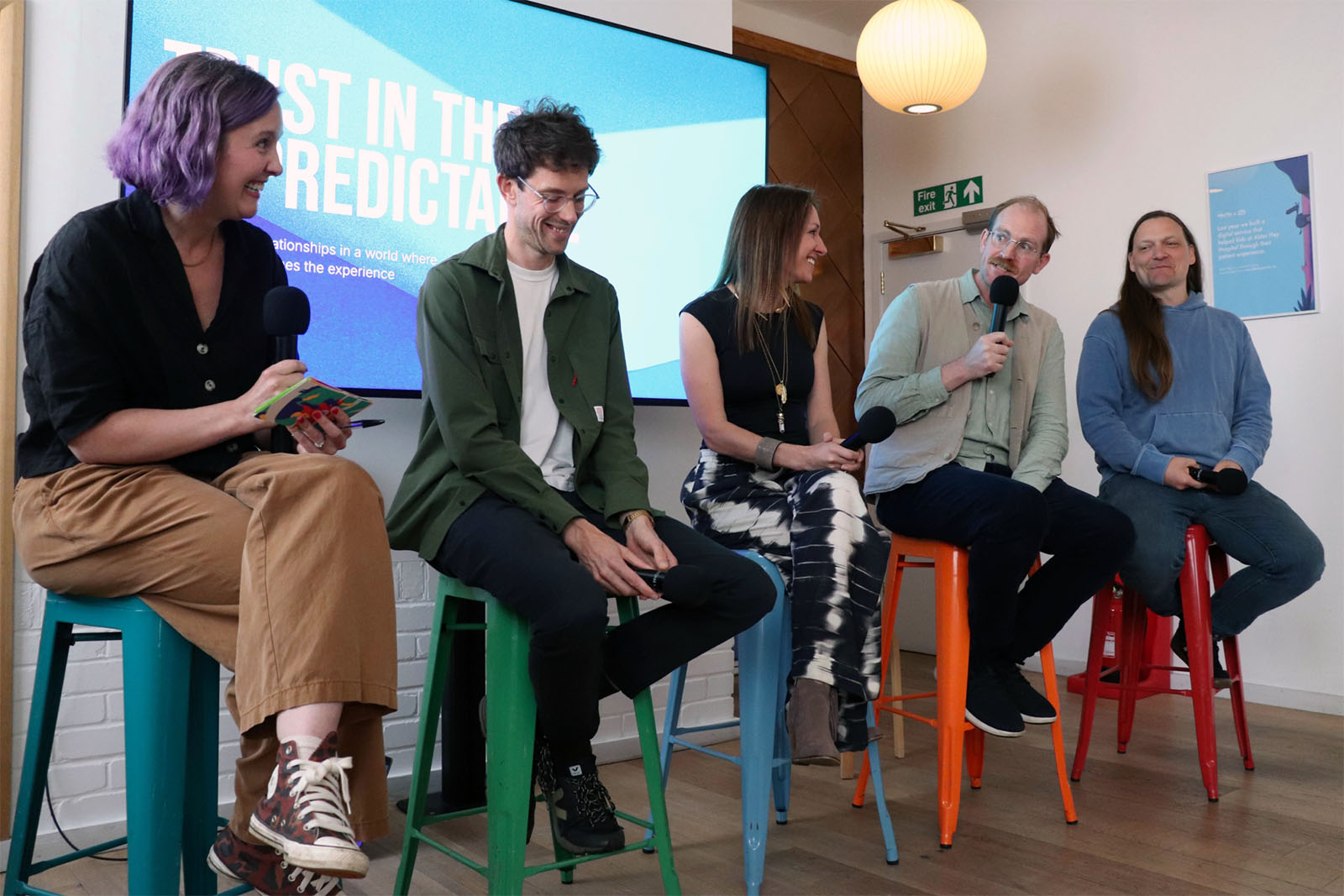Five panellists sitting on chairs with ‘Trust in the unpredictable’ on the screen behind them.