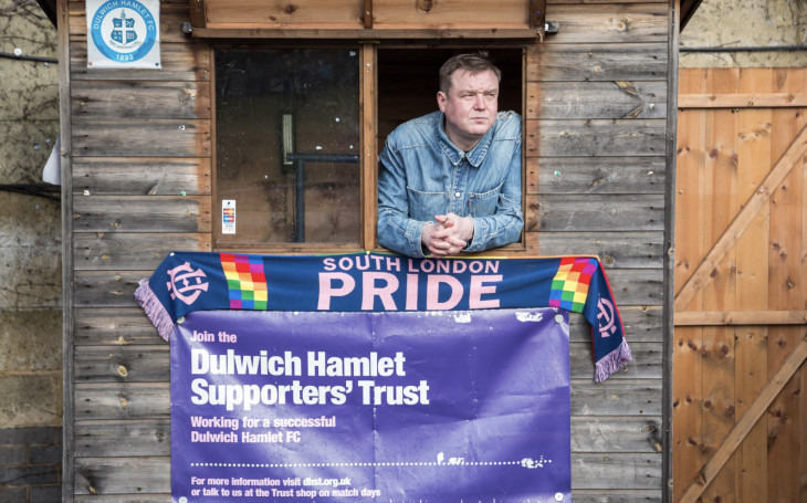 A member of the Dulwich Hamlet Supporters' Trust standing next to a 'South London Pride' scarf