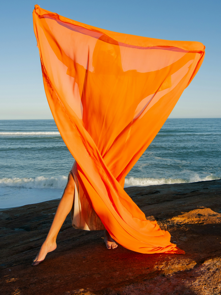 Frau mit orangenem Tuch am Strand.