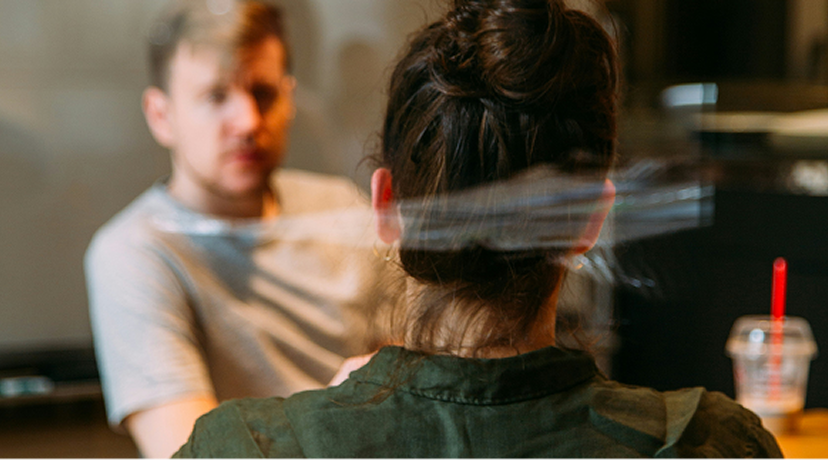 Mann und Frau unterhalten sich hinter einer Glaswand