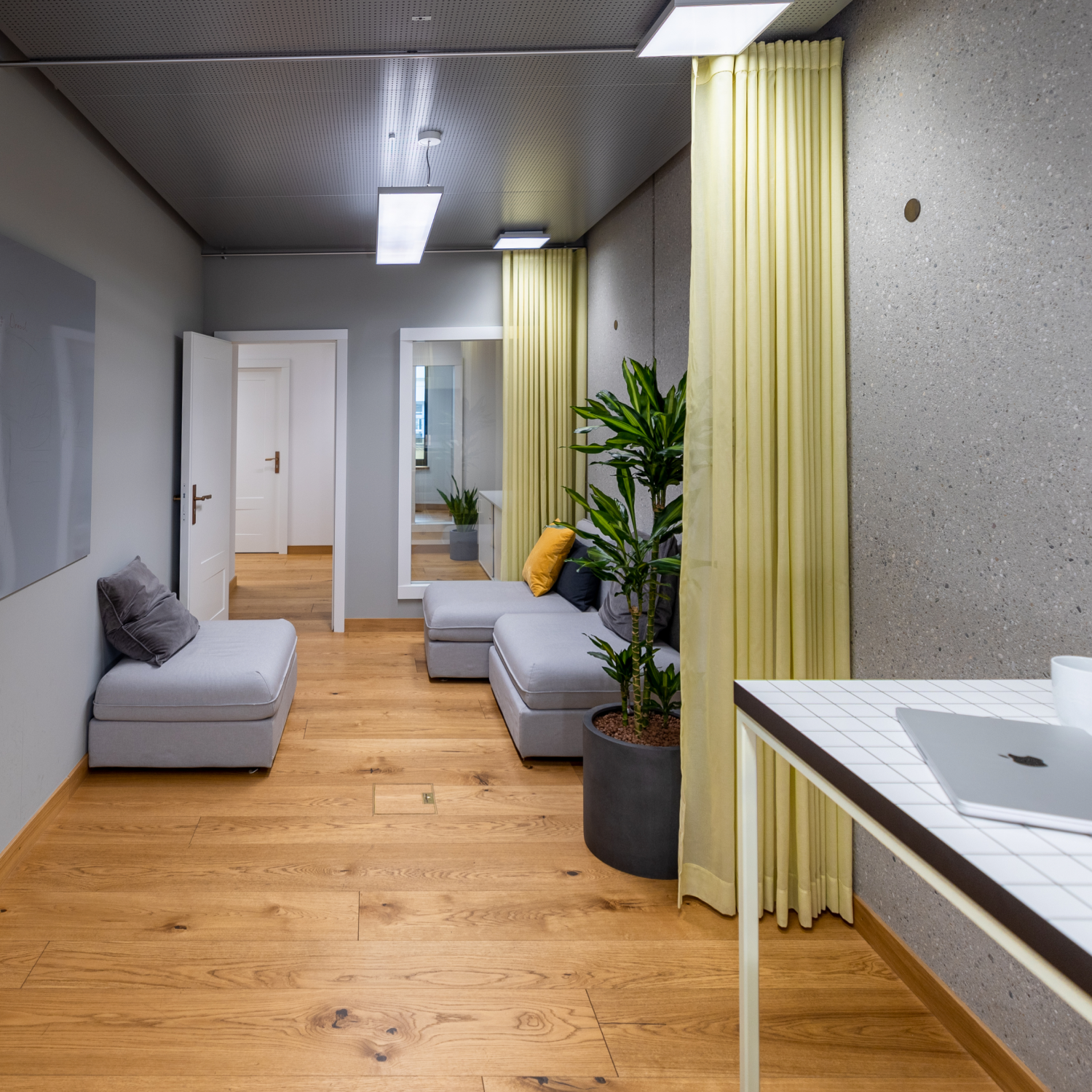 Coworking Space mit Sofas, gelben Vorhängen und Stehtisch im Vordergrund