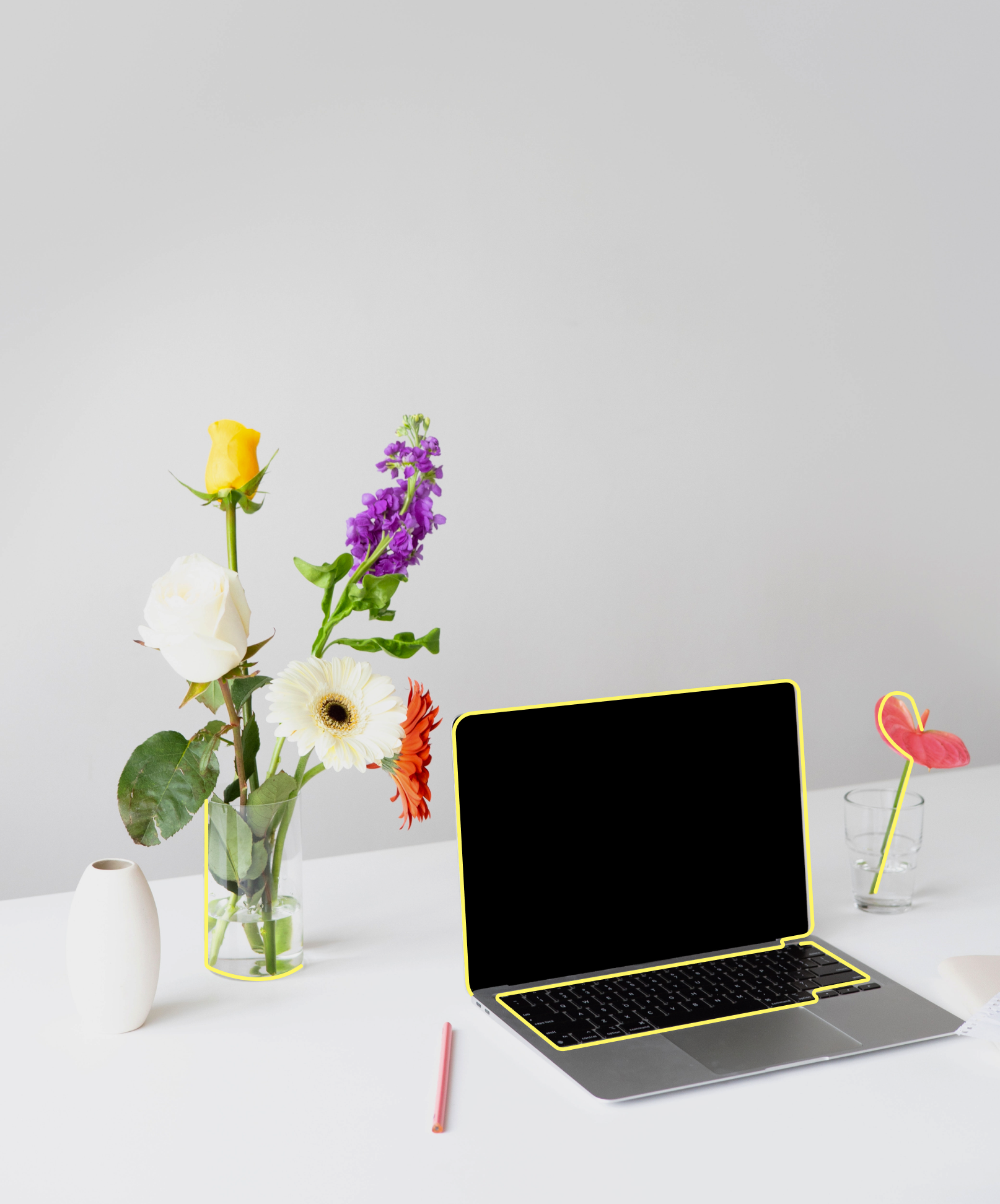 Ein Laptop steht auf einem weißen Tisch in Umgebung von bunten Blumen