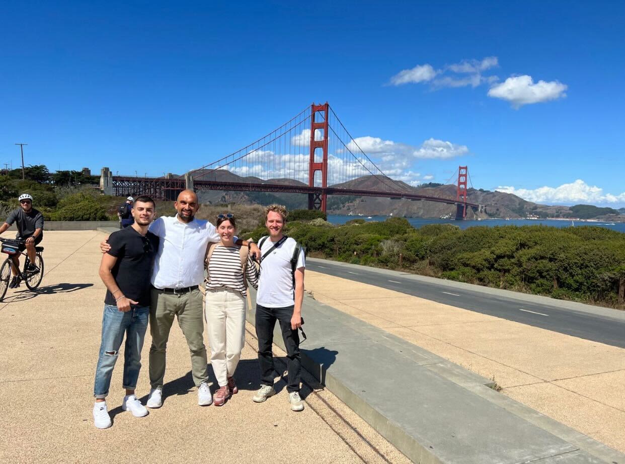 A group of people look into the camera on sunny day. In the background is the Golden Gate Bridge.