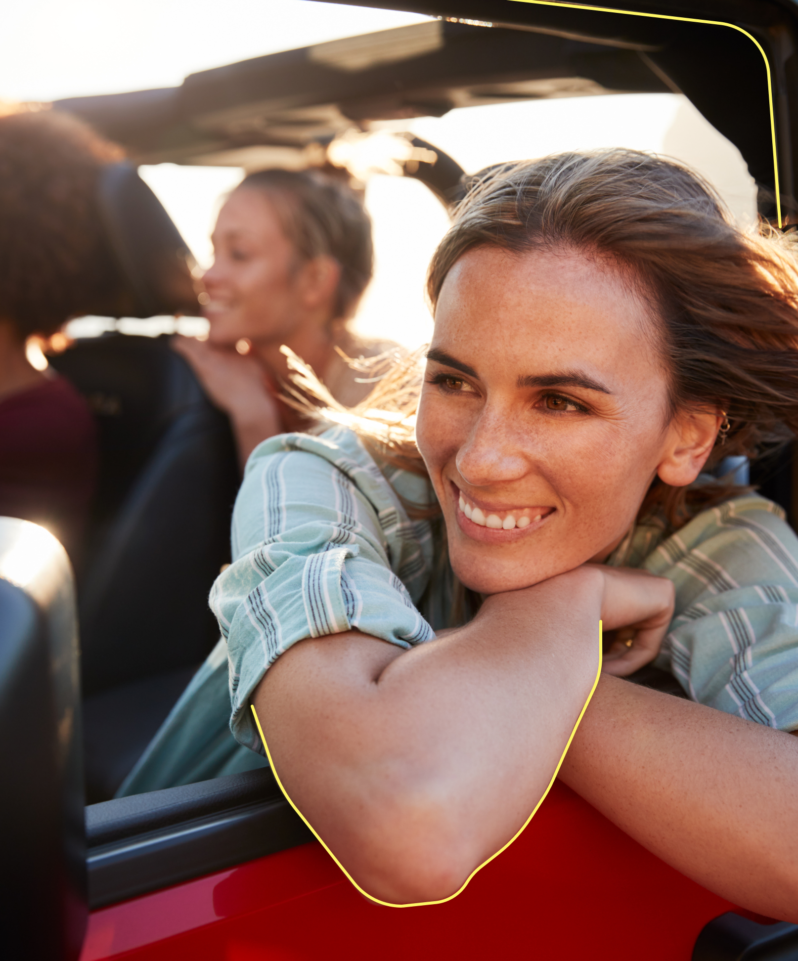 Eine Frau lehnt sich an das Fenster eines fahrenden Autos und lächelt breit, als der Wind ihr entgegenweht