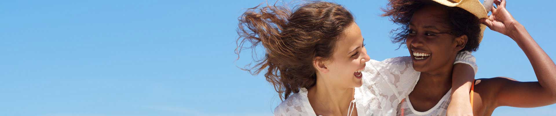Zwei Frauen am Strand, die spazieren gehen, reden und lächeln