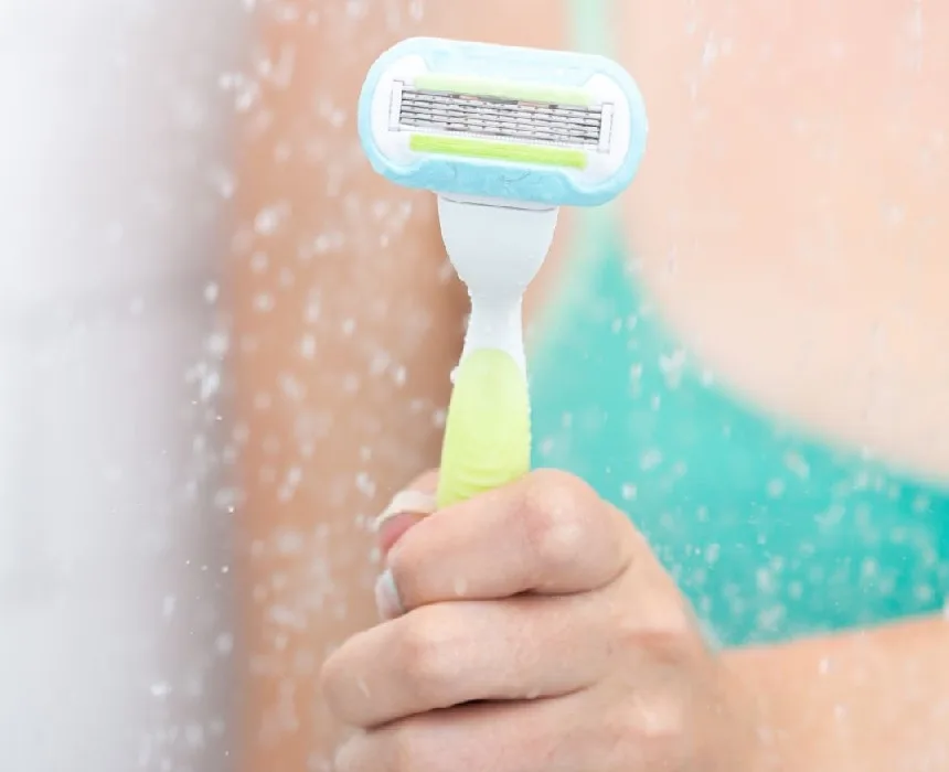 Frau hält Rasiermesser unter der Dusche
