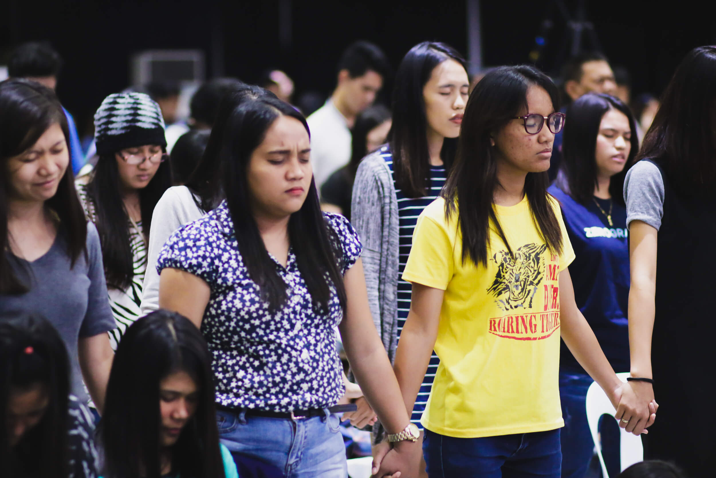 People in the audience holding hands and closing their eyes to pray.