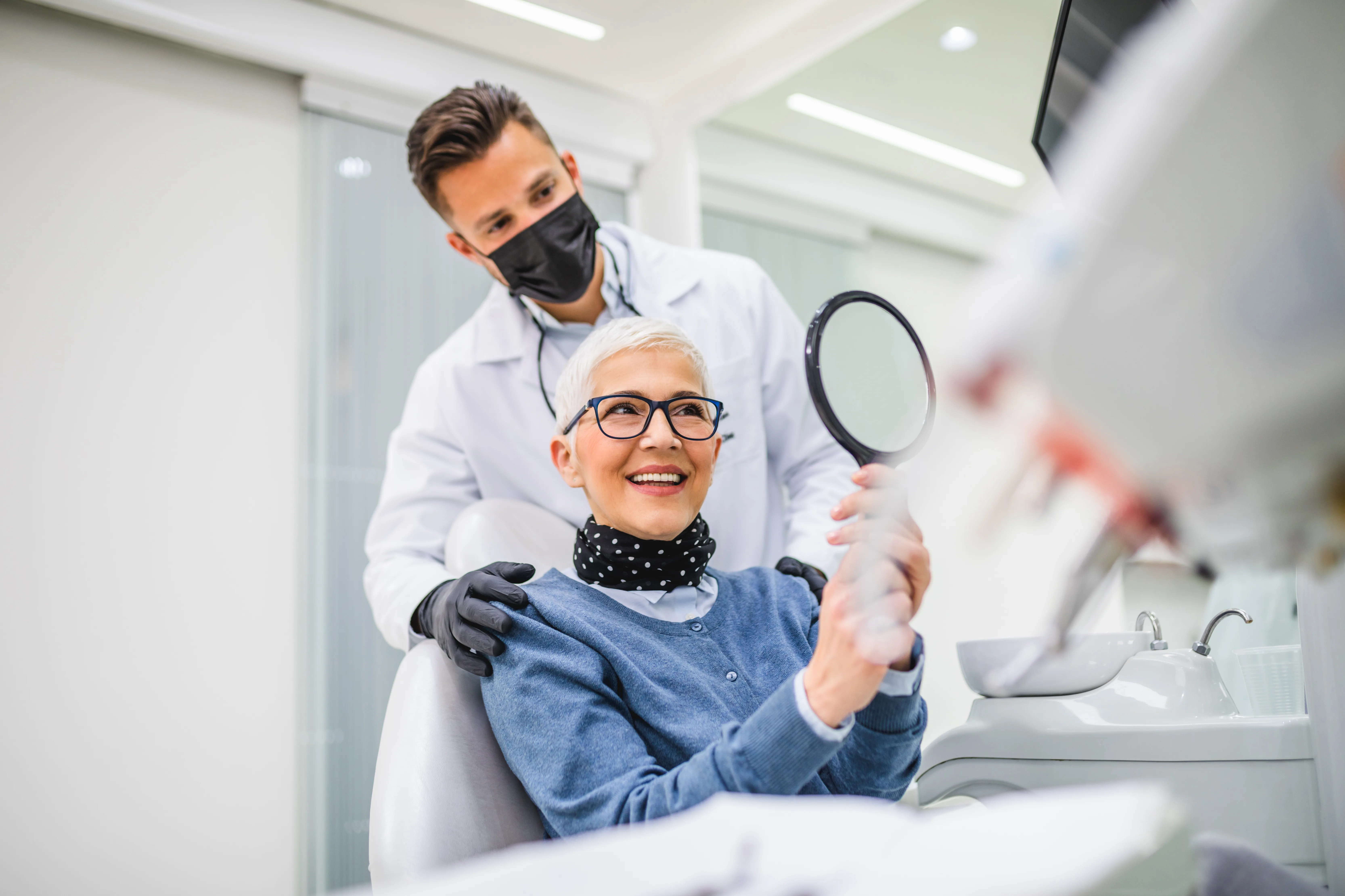 Dentista e paziente sorridono allo specchio.