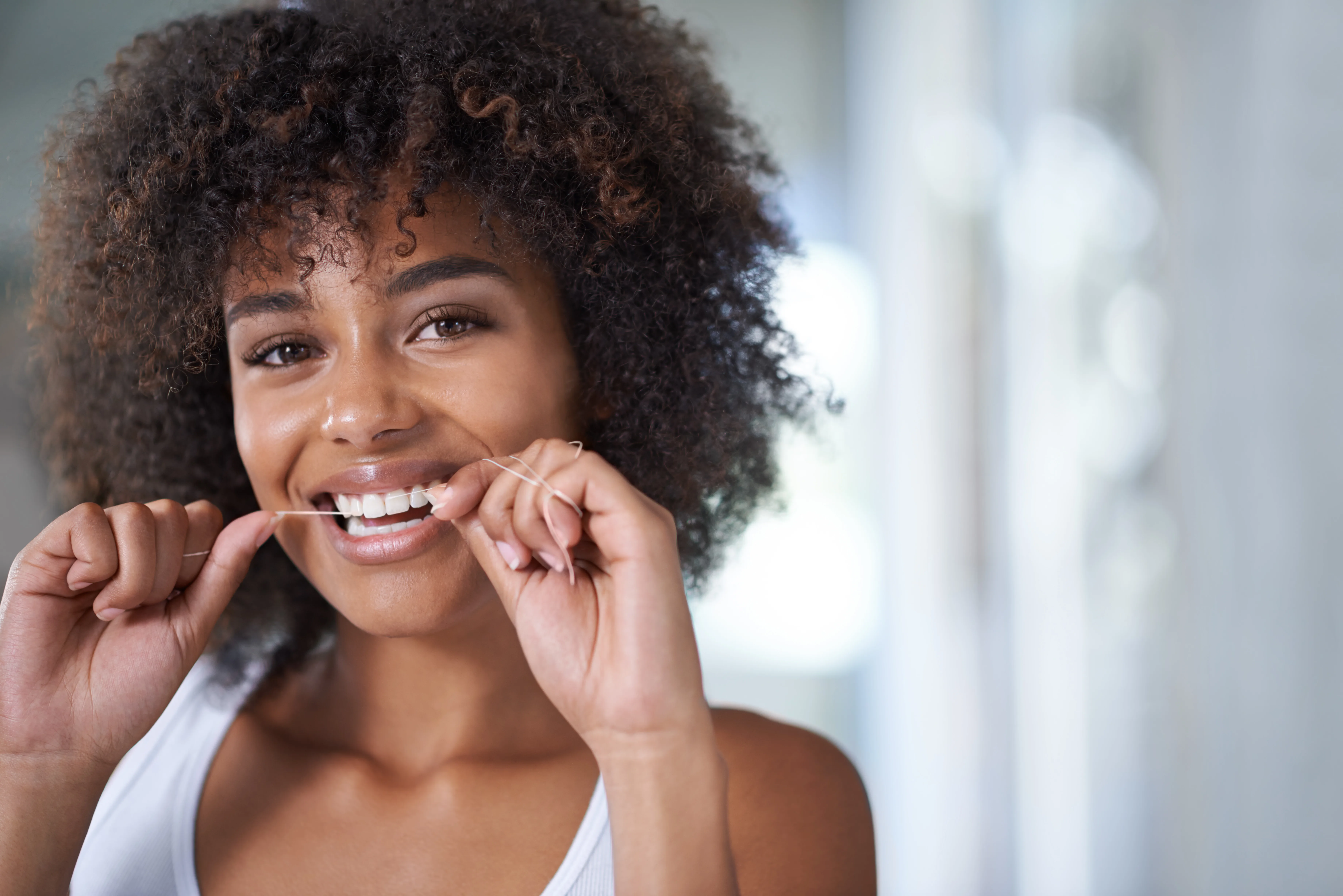 Donna in bagno che sorride e passa il filo interdentale sui suoi denti bianchi.