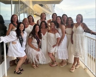 Group of 13 female friends in white dresses on a cruise deck.