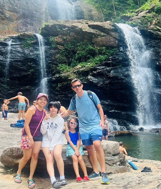 Family posing in front of High Falls waterfall with trees in the background