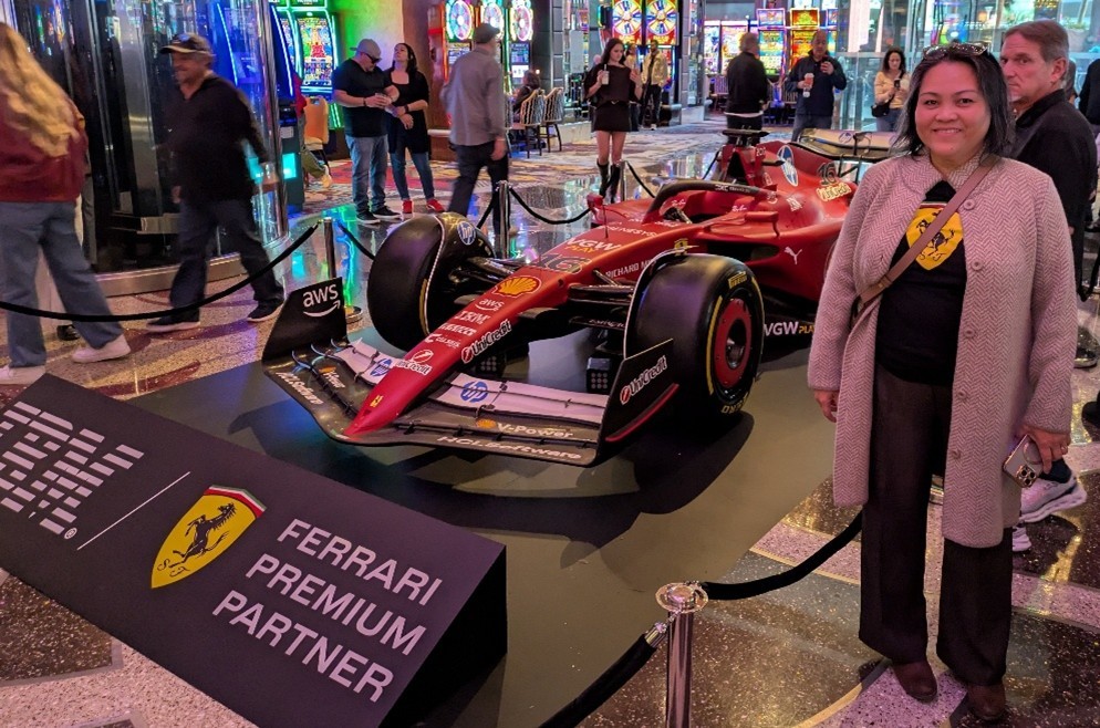 Smiling woman standing beside a racing car exhibit with a crowd in the background