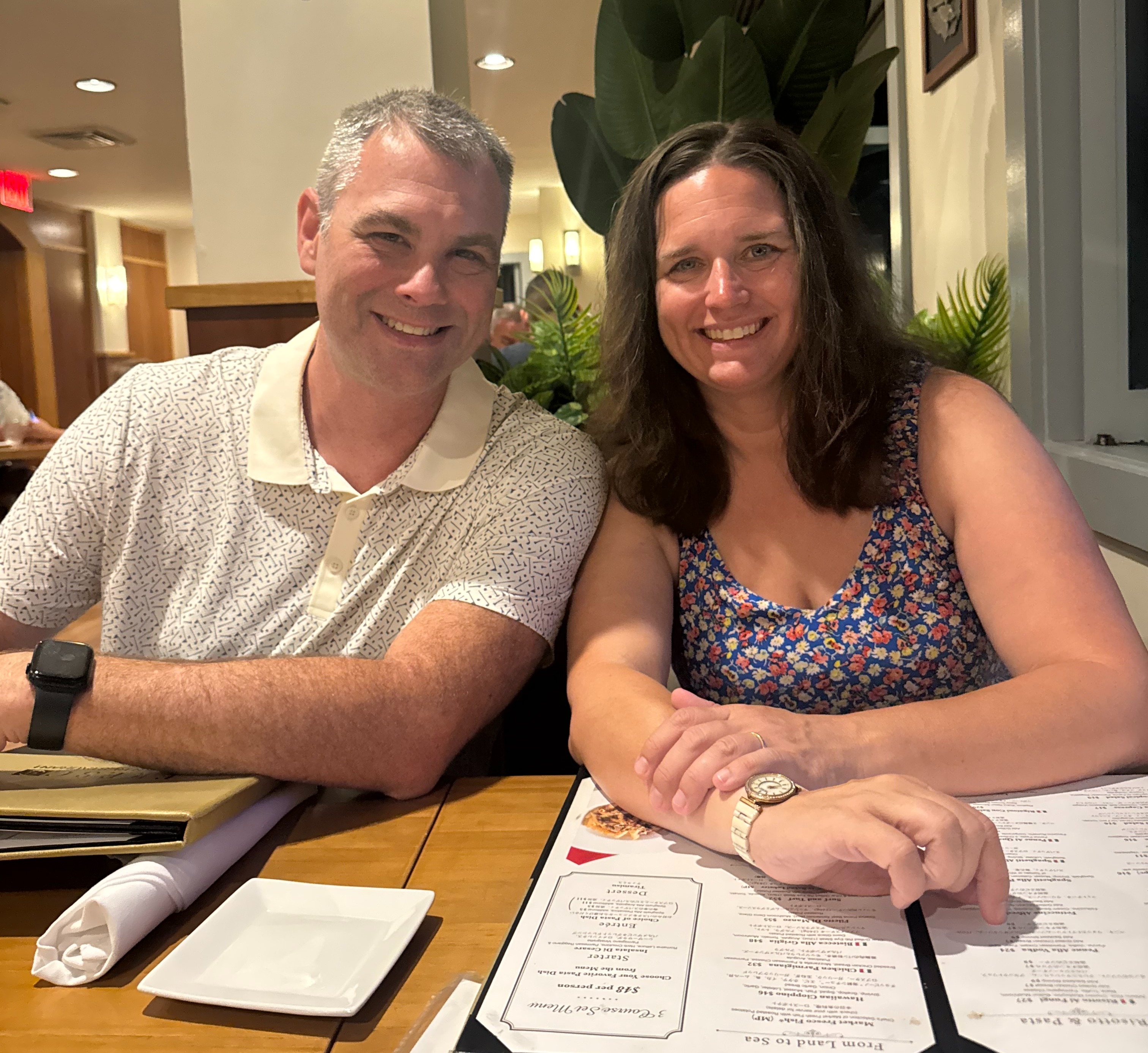 Couple smiling, sitting in a restaurant with menus.&nbsp;