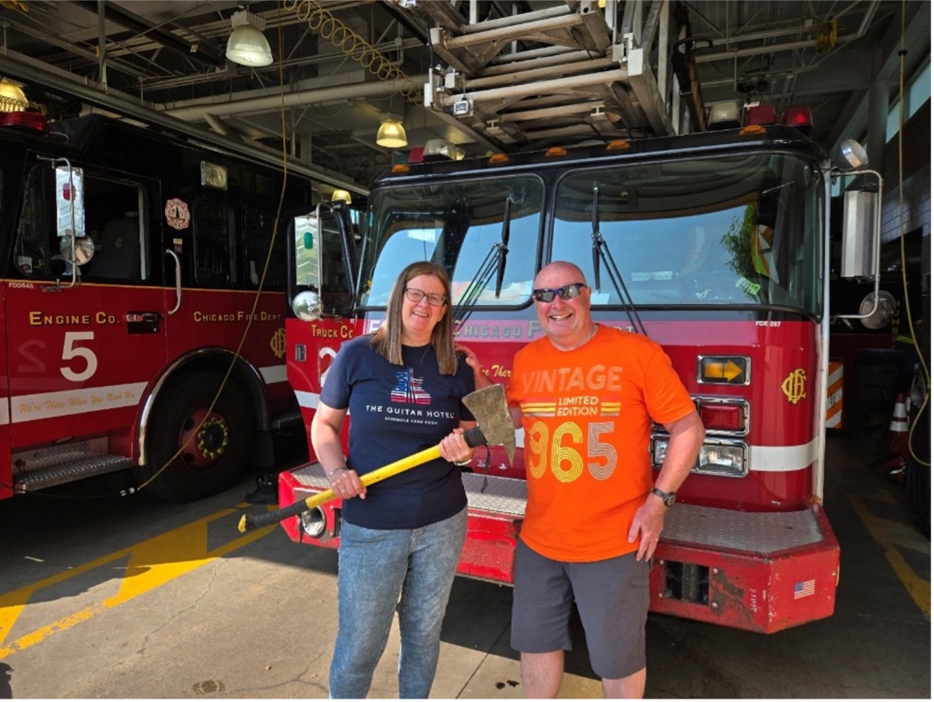 Smiling couple standing in front of a Chicago firetruck with the woman holding a flat-head axe