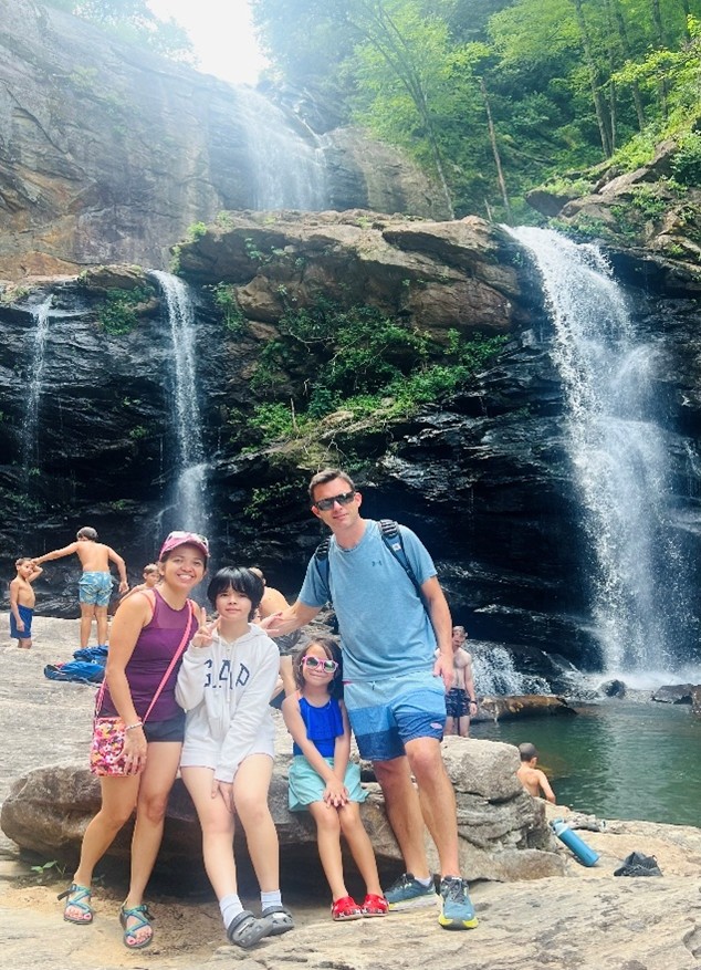 Family posing in front of High Falls waterfall with trees in the background.
